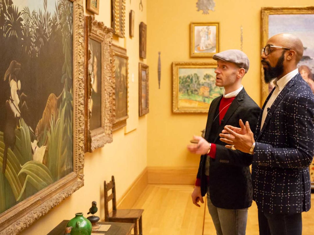 two men look at paintings hanging on a gallery wall
