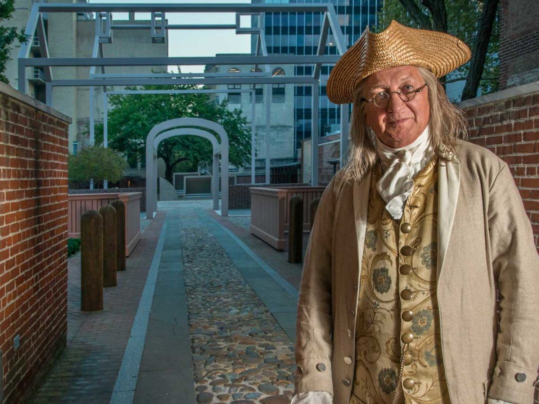 a man dressed as Ben Franklin poses at the entrance to the museum grounds