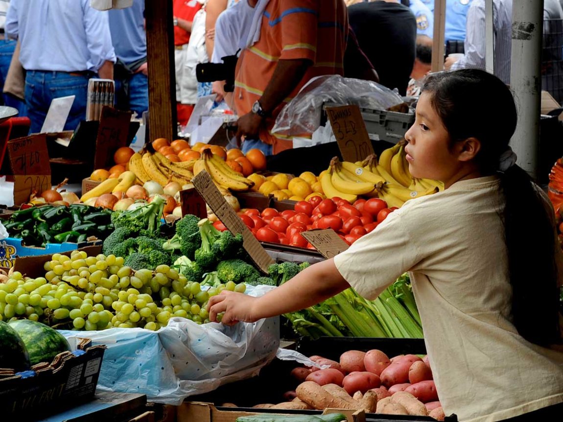 a girl stands by cases of produce in an open-air market