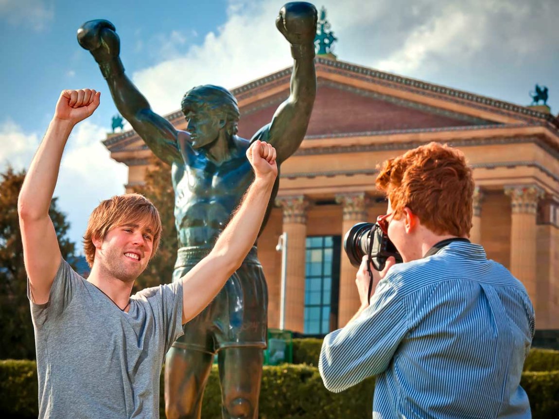 a photographer captures a young man posing in front of Rocky with his arms upraised