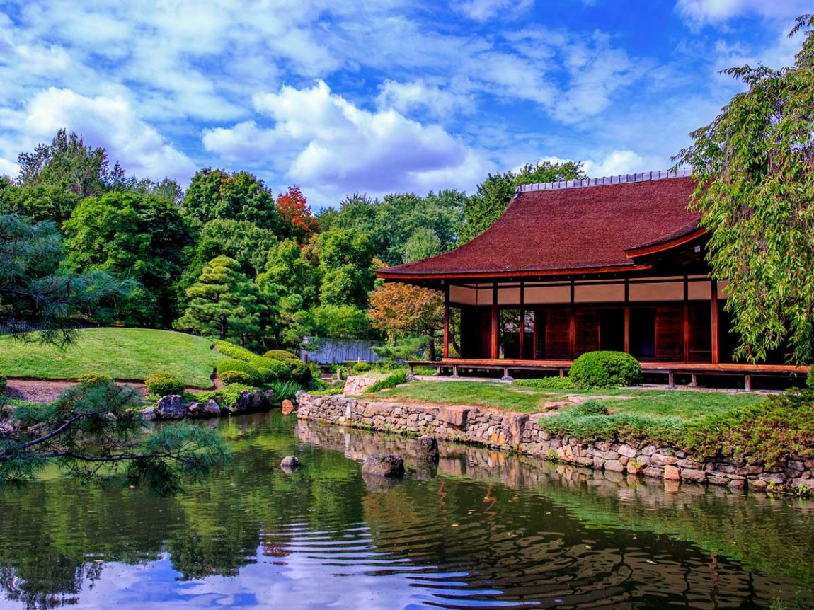 a Japanese-style pavilion next to a pond, surrounded by greenery
